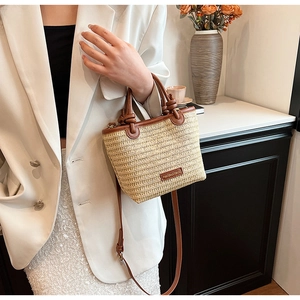 Close-up of beige straw bag with brown leather trim and metal logo plate on the side