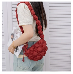 Close-up of a dark red quilted cloud bag with puffy nylon texture and pleated strap