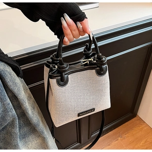 Close-up of woven cream bucket bag with black leather trim and metal brand logo detail