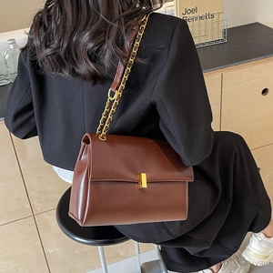 Brown leather chain tote bag with gold metal buckle and shoulder strap in a lifestyle setting