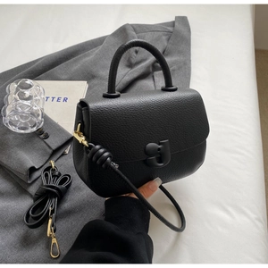 Détail d'un sac à main en cuir grainé noir avec finitions dorées sur un blazer gris
