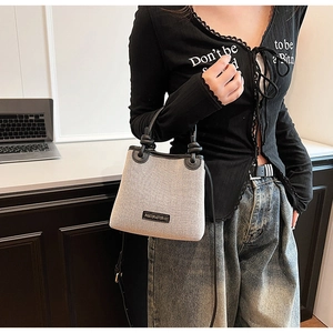 Detail of a large beige canvas bucket bag with black leather trim and top handle for commuting
