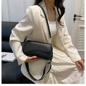 Détail du sac bandoulière noir avec rabat ondulé et sangle déco sur un mannequin chic
