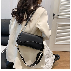 Détail d'un sac bandoulière en cuir noir avec double sangle porté par un mannequin chic