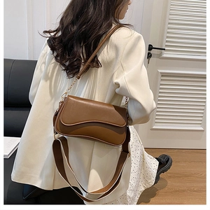 Détail d'un sac bandoulière marron en cuir avec rabat ondulé et large sangle en toile