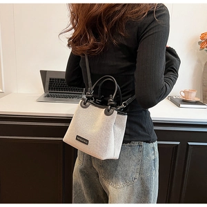 Detail view of small bucket bag in cream canvas with black leather trim and top handle