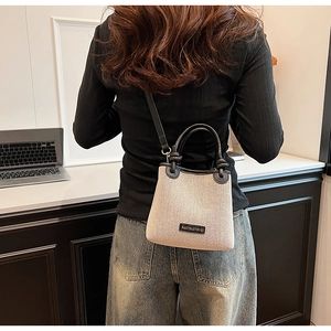 Detail showing the beige canvas bucket bag with black leather straps and metal logo plate