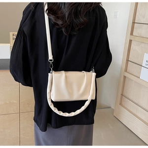 Detail of a creamy beige pleated crossbody bag with a soft handle and adjustable strap