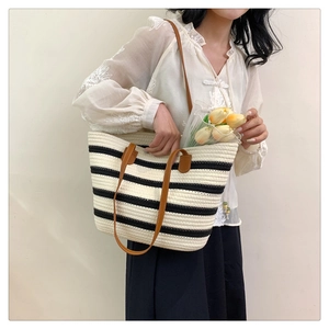 Detail of a black and white striped woven tote bag with leather straps and flowers