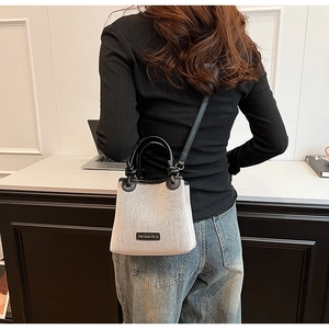 Detail of a woven bucket bag with black leather straps worn by a model in office setting