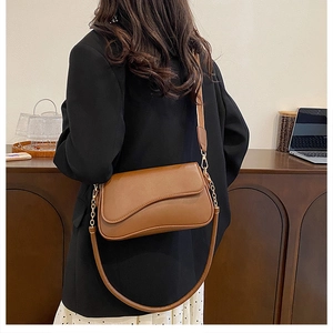 Sac bandoulière en cuir marron avec rabat asymétrique et chaîne dorée sur mannequin