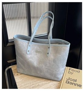 Close-up of light blue suede tote bag featuring silver rivets and metal logo detail