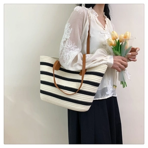 Detail of woven striped tote bag with brown leather handles held by a model with tulips