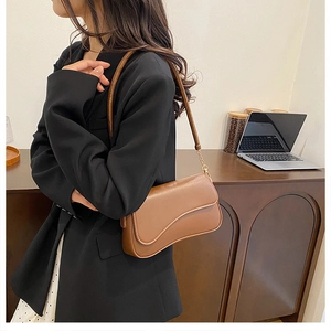 Détail du sac en cuir marron avec rabat incurvé et chaîne dorée sur le mannequin