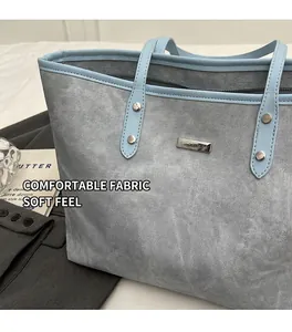 Detail of light blue textured tote bag with metal brand logo and reinforced rivets