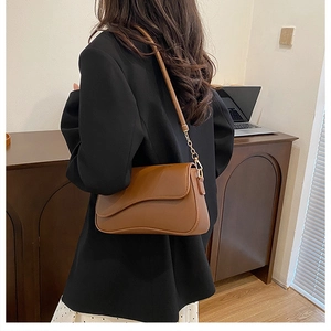 Détail d'un sac bandoulière marron mat avec chaîne dorée et rabat au design incurvé