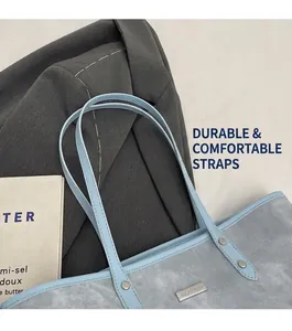 Close-up of light blue tote bag featuring metallic brand plate and leather shoulder strap