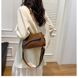 Détail d'un sac bandoulière marron en cuir avec sangle rayée et garnitures dorées