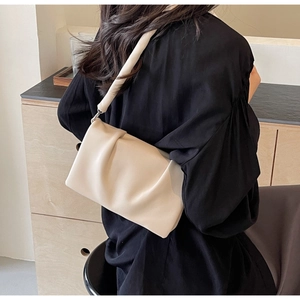 Detail of a creamy white pleated shoulder bag worn by a model in a minimalist room
