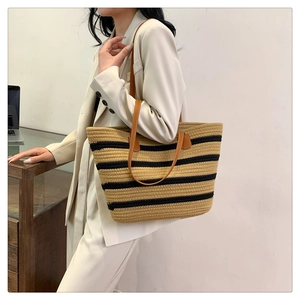 Detail of hand-woven tote bag with black stripes and brown leather straps on a shoulder