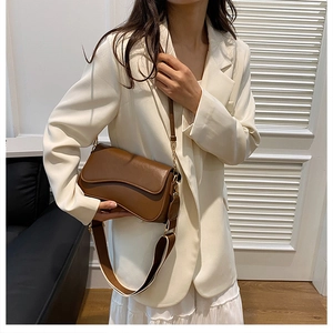 Sac bandoulière en cuir marron avec deux sangles porté par un mannequin en tenue blanche