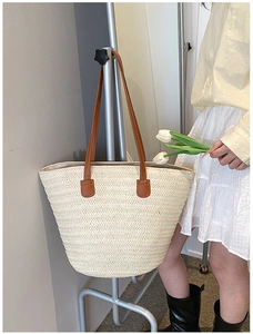 Close-up of large straw tote bag with woven texture and brown leather shoulder straps