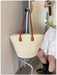 Close-up of woven straw tote bag featuring brown faux leather straps and reinforced stitching