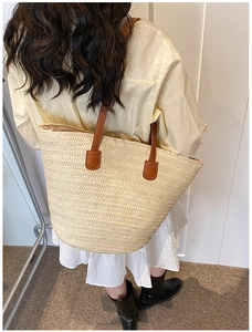 Detail of large woven straw tote bag with brown leather straps shown on a model