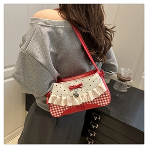 Detail view of red plaid shoulder bag with lace edges and heart pendant on a model