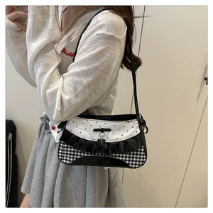 Detail of checkered shoulder bag with black bow, heart charm, and ruffled lace trim