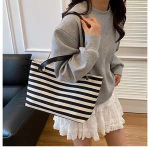 Detail view of black and white striped canvas tote bag with black leather shoulder strap