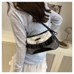 Close-up of black and white lace baguette bag with heart pendant and ruffled trim detail