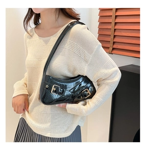 Detail of black glossy crocodile embossed shoulder bag with gold buckles on model