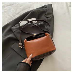Detailed shot of two-tone crossbody bag with orange pleated texture and brown leather strap