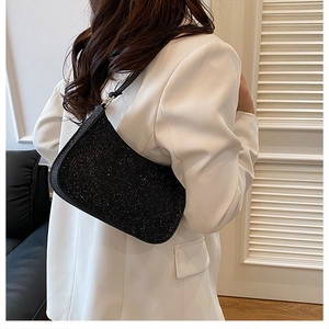 Detailed close-up of a black sequined baguette underarm bag on a white blazer background