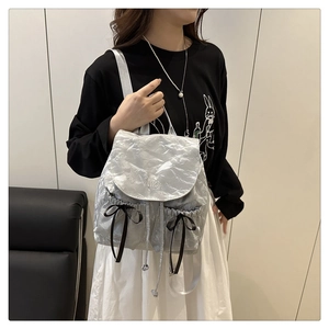Détail du sac à dos argenté froissé avec poches ornées de nœuds noirs élégants