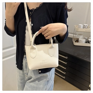 Detail of a creamy white lychee grain faux leather crossbody bag with DX logo engraving