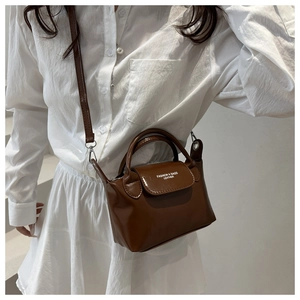 Détail d'un mini sac à bandoulière marron avec poignée et texte mode sur le rabat
