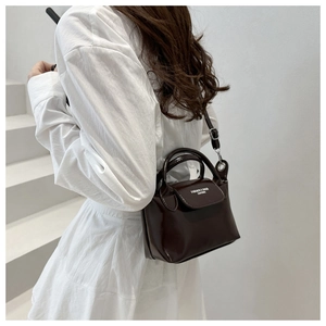Model wearing dark brown glossy leather crossbody bag against a white minimalist backdrop