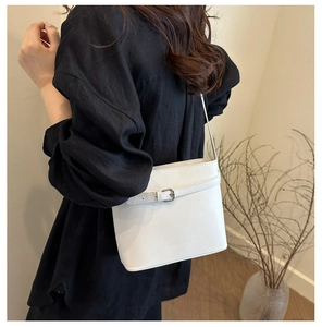 Close-up of minimalist white leather bucket bag with buckle and embossed logo