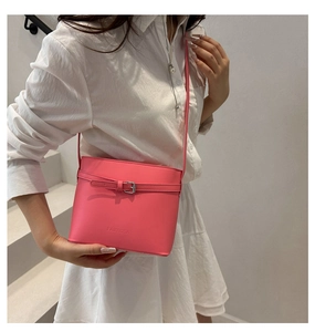 Detail of bright pink leather crossbody bag showing buckled strap and embossed logo texture