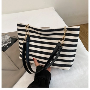 Detail of striped tote bag featuring metal chain and black leather spliced handles