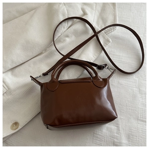 Detail of a brown small dumpling bag showing glossy faux leather texture and silver hardware