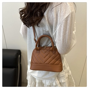 Bolso tipo concha marrón acolchado con costuras en V llevado como bandolera en modelo