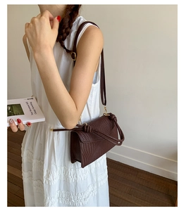 Détail du sac bandoulière tressé marron foncé avec sangle à nœud et détails dorés