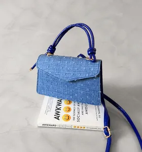 Detail einer blauen Denim-Handtasche mit 3D-Pompon-Textur und blauen Seilriemen auf Stuhl