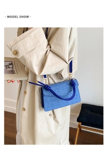 Detail of blue textured crossbody bag with gold hardware shown with a beige trench coat