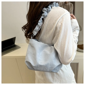 Detail of light blue crossbody bag featuring ruffled strap and bear label on fabric