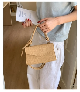 Détail d'un sac à main tissé marron clair avec texture en V et poignée à nœud élégante