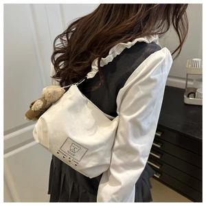 Detail of white canvas dumpling bag featuring pleated strap and cute brown bear charm